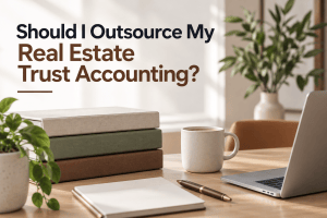 Should I outsource my real estate trust accounting? Blog header with laptop, folders, notebook and coffee on a modern office desk.